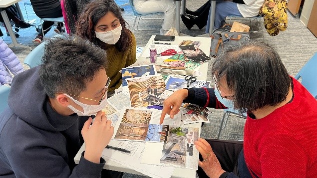Women and men wearing masks over their noses and mouths studying photos laid out on a table.